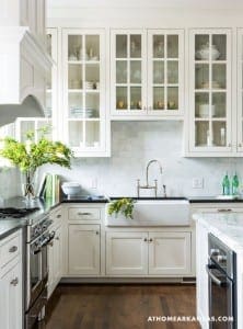 White kitchen cabinets with glass-front display, farmhouse sink, and marble countertop.