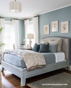 Blue bedroom with a gray bed, white curtains, and framed botanical prints.