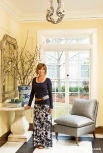 Woman stands before a console table with a large mirror and floral arrangement.
