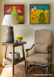 Two framed paintings, a table lamp, and a chair in a room.