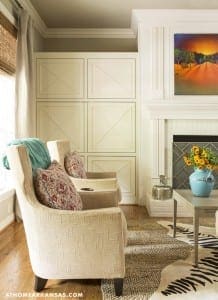 Cream-colored built-in cabinets with a landscape painting, armchair, and floral vase.