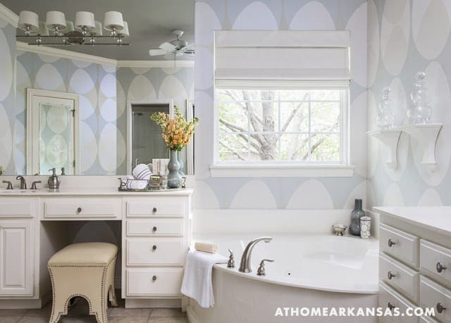 Bathroom with patterned wallpaper, vanity, tub, and window.