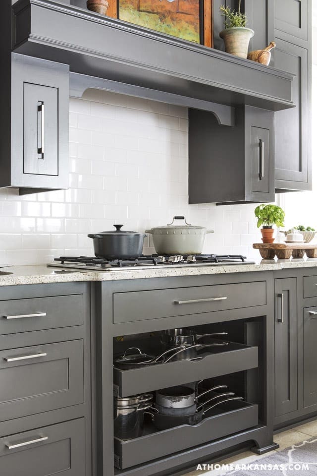 Gray kitchen cabinetry with white subway tile and a stovetop.