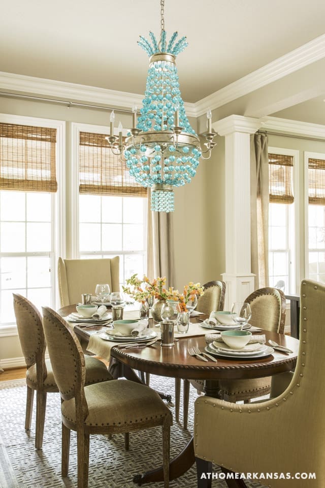 Dining room with a turquoise chandelier, wooden table, and upholstered chairs.