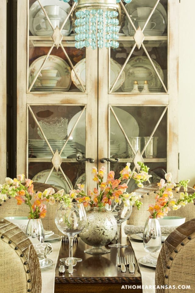 White cabinet with glass doors and turquoise accents, floral arrangement.