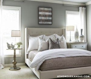 Gray bedroom with a tufted headboard, white curtains, and a wooden sign.