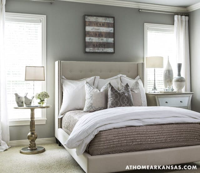 Gray bedroom with a tufted headboard, white curtains, and a wooden sign.