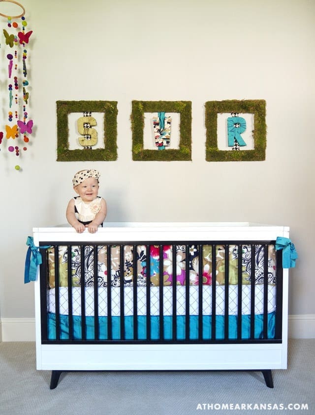 Crib with patterned bedding and moss-covered framed letters.