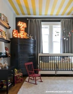 Striped ceiling with yellow and black, featuring a large light fixture and nursery furniture.