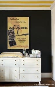 White dresser with yellow and black accents, featuring a movie poster and storage basket.