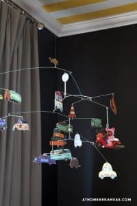 Dark wall with gray curtains and mobile featuring toy vehicles.