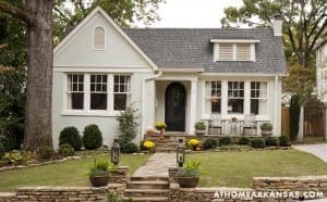 White cottage with dark roof, landscaping, and porch.