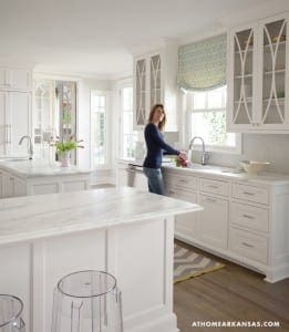 White kitchen with marble island and woman arranging flowers.