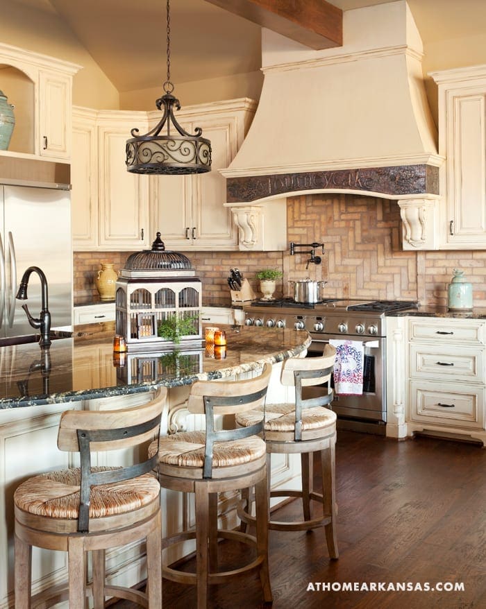 Cream kitchen with brick backsplash, wood bar stools, and a large pendant light.