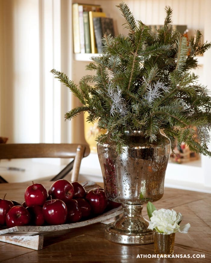 Silver urn with pine branches, apples, and white flowers.
