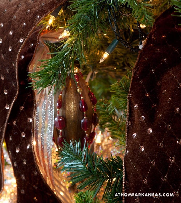 Brown velvet ribbon with lights and red beads on a Christmas tree.