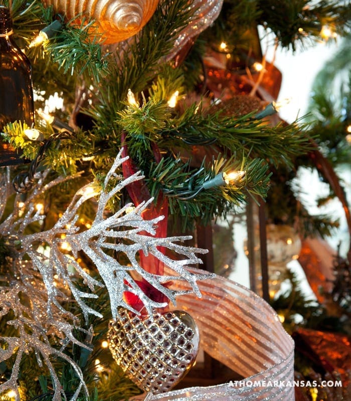 Silver and red Christmas ornament on decorated tree branch.