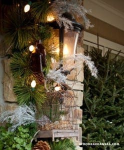 Stone pillar decorated with pine garland, lights, and a birdcage.