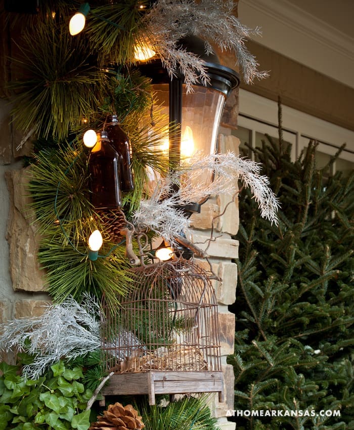 Stone pillar decorated with pine garland, lights, and a birdcage.