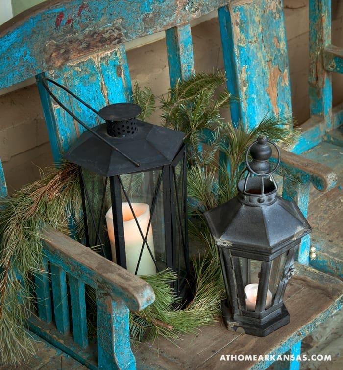 Blue wooden bench with two black lanterns and greenery.