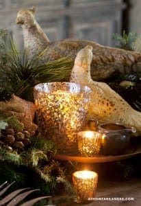 Gold statue, candle holders, and greenery on a wooden tray.