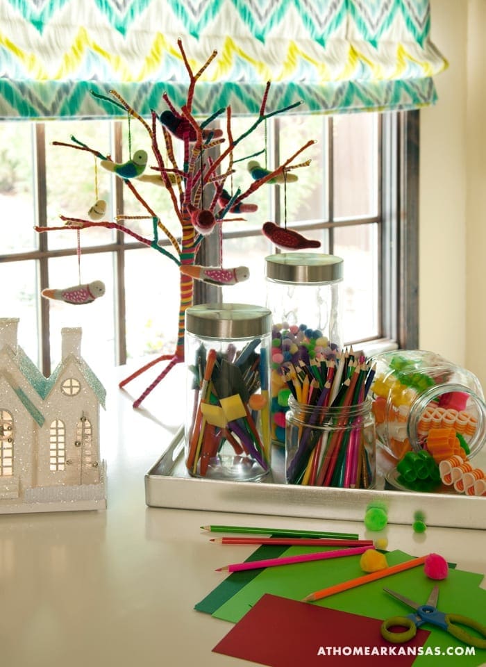 Fabric window shade with teal and zigzag pattern, decorated tree with birds, and art supplies.