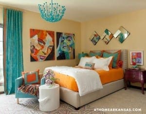 Bedroom with teal and orange accents, artwork, and a chandelier.