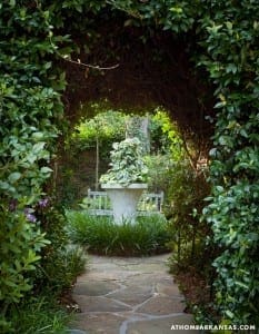 Stone pathway through a leafy green archway in a garden.