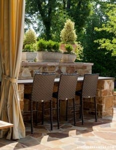 Stone outdoor kitchen with seating and beige curtains.