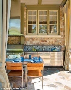 Outdoor kitchen with stone facade, windows, and a wooden table.