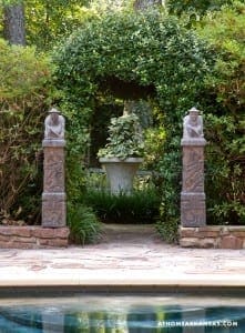Stone columns and hedges frame a pool area.