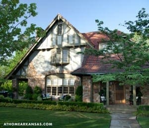 Stone Tudor-style house with red tile roof, trees, and a lawn.