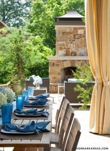 Stone outdoor fireplace with patio furniture and blue tableware.