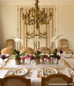 Gold chandelier and ornate wall paneling with orchids and table setting.