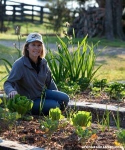 Woman kneeling in garden with leafy greens and spring flowers.