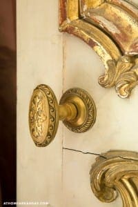Gold-toned decorative door handle on white paneling.