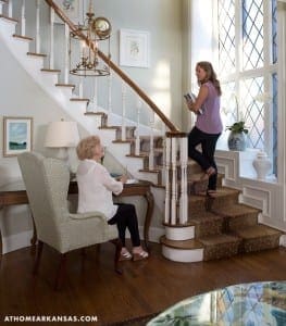 White staircase with a woman and girl, wooden floors, and a chandelier.