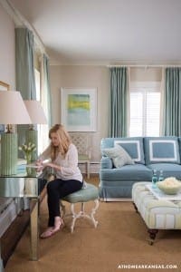 Blue sofa, teal curtains, and a woman writing at a mirrored desk.