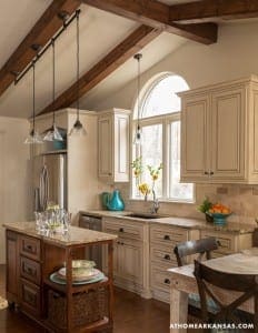 Kitchen with exposed wooden beams, pendant lights, and cream cabinets.