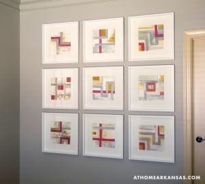 Nine framed abstract paintings on a gray wall.
