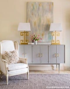 Gray sideboard with gold accents, flanked by lamps and a chair.