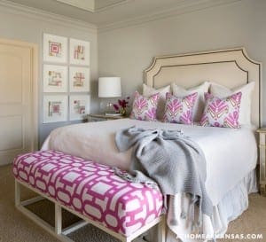 Cream upholstered bed with pink and gray pillows, bench with patterned upholstery.