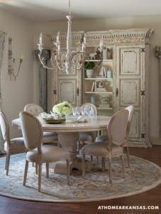 Cream-colored dining room with a large chandelier and antique cabinet.