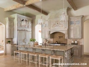 Large kitchen with light gray cabinets, marble island, and decorative chandeliers.