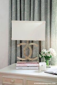 White lamp on patterned wallpaper with books and flowers.