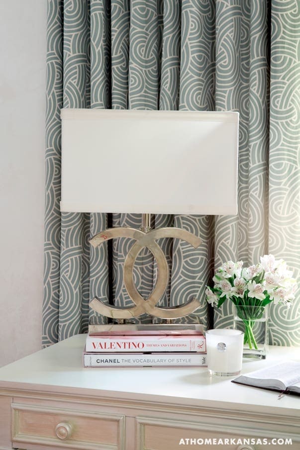White lamp on patterned wallpaper with books and flowers.