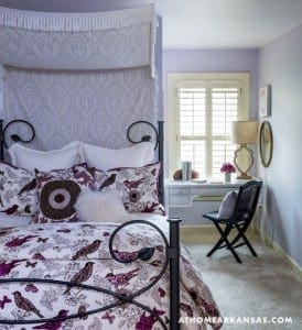 Purple bedroom with a canopy bed, patterned wallpaper, and a gray desk.