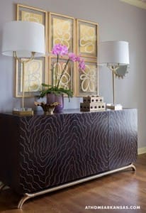Dark wood console table with patterned upholstery and gold lamps.