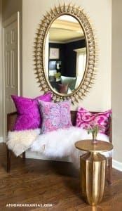 Oval mirror with golden spikes, pink pillows, and a wooden side table.