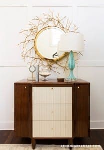 Dark wood cabinet with white and teal accents, gold mirror and lamp.